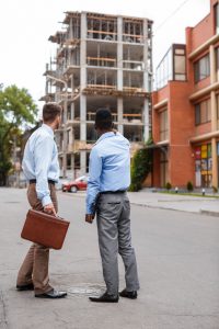 African-American businessman and a Caucasian businessman discussing a construction project on the background of building a house
